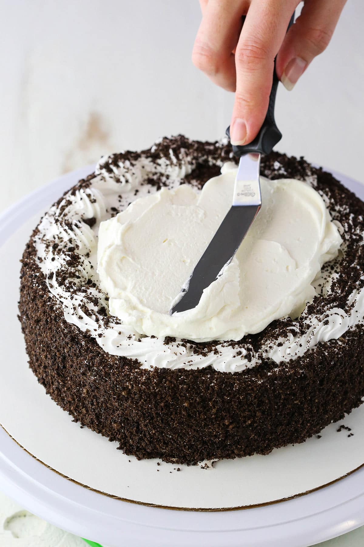 Spreading white frosting on an Oreo Ice Cream Cake with an offset spatula