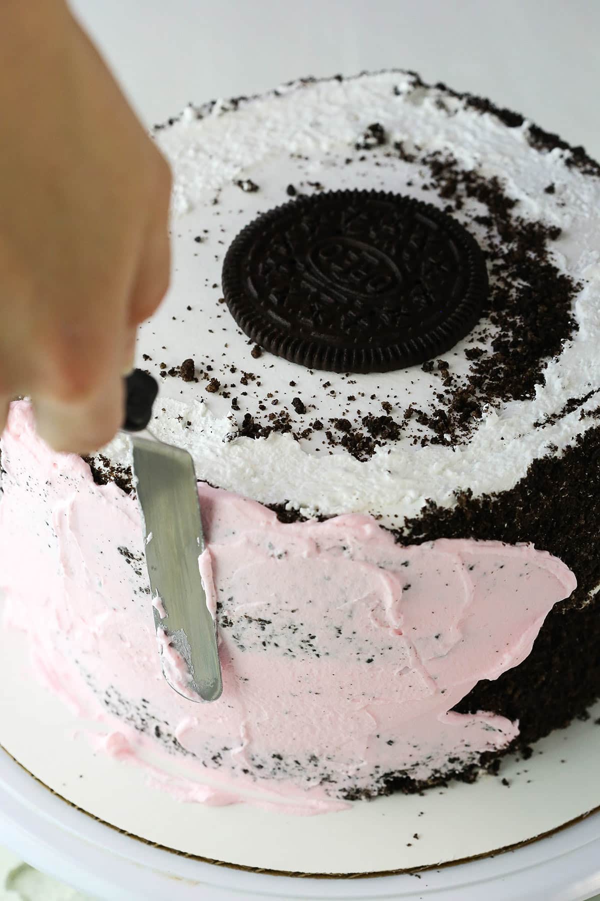 Spreading pink frosting on an Oreo Ice Cream Cake with an offset spatula