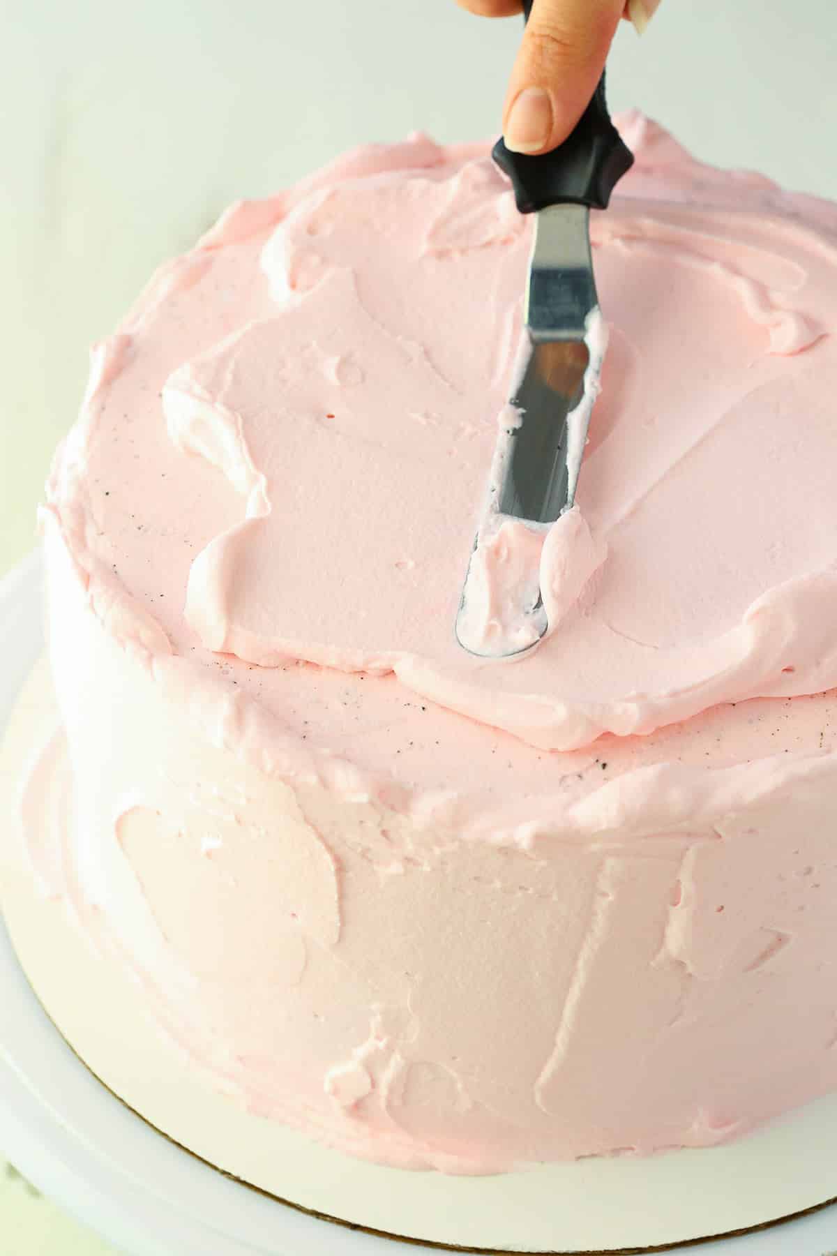 Spreading pink frosting with an offset spatula on an Oreo Ice Cream Cake