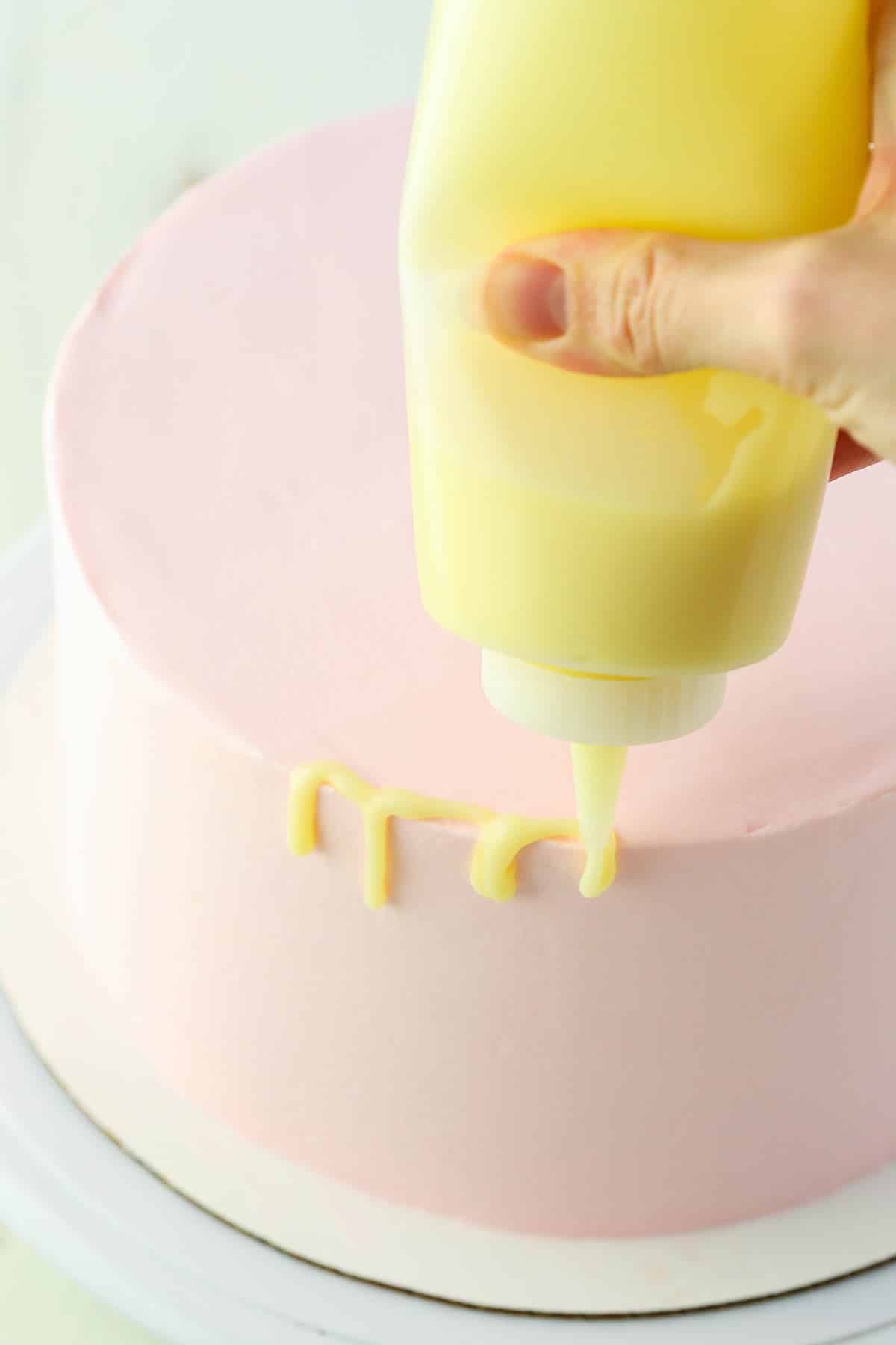 Dripping white chocolate ganache on a pink cake using a squeeze bottle