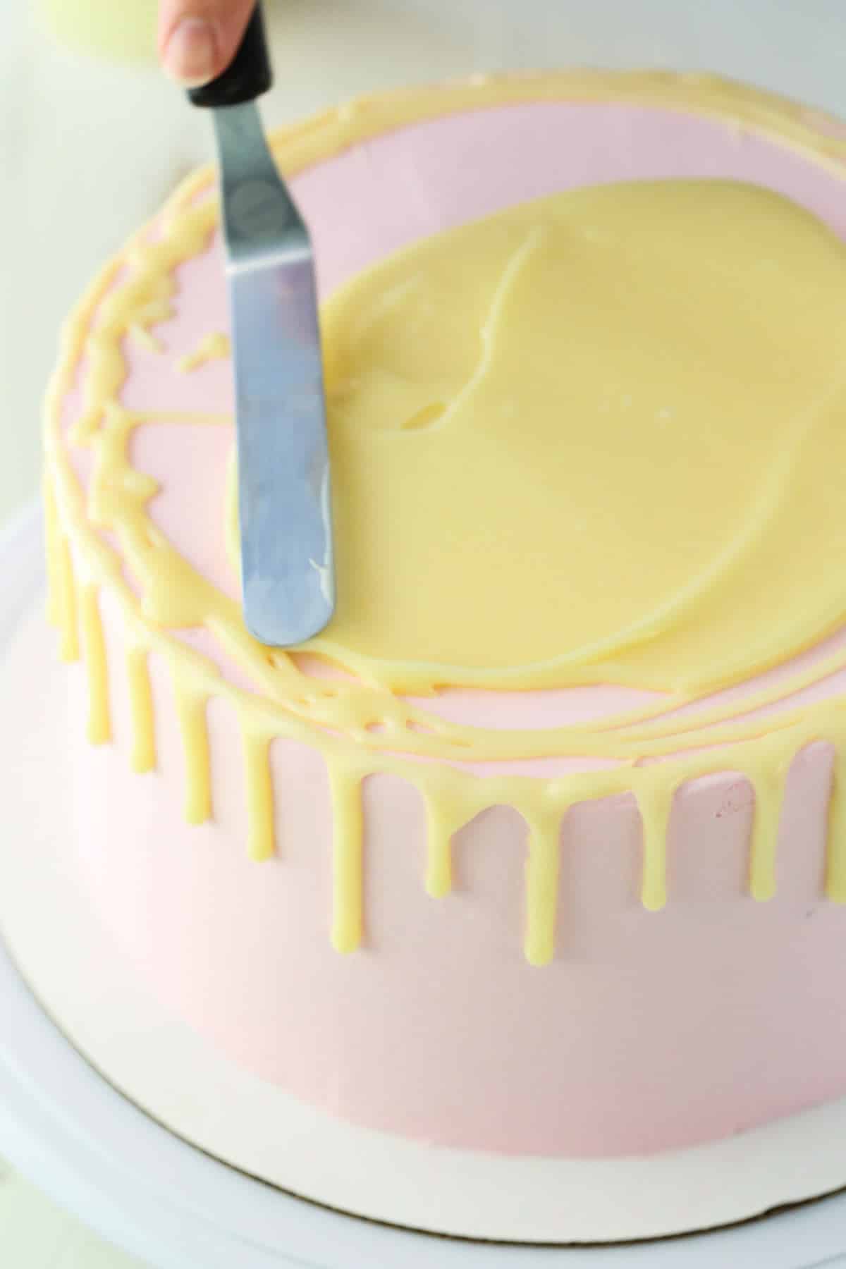 Spreading white chocolate ganache on the top of a pink cake using an offset spatula