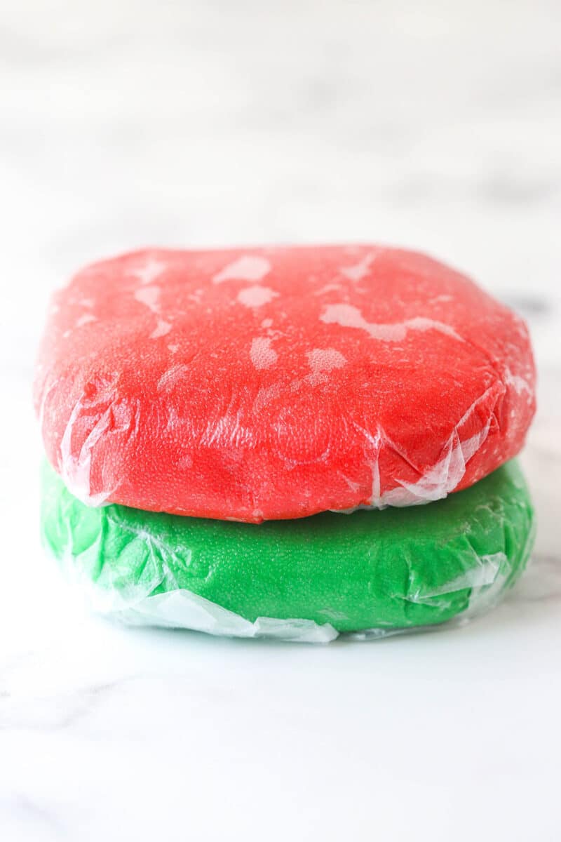 Balls of red and green cookie dough wrapped in plastic wrap