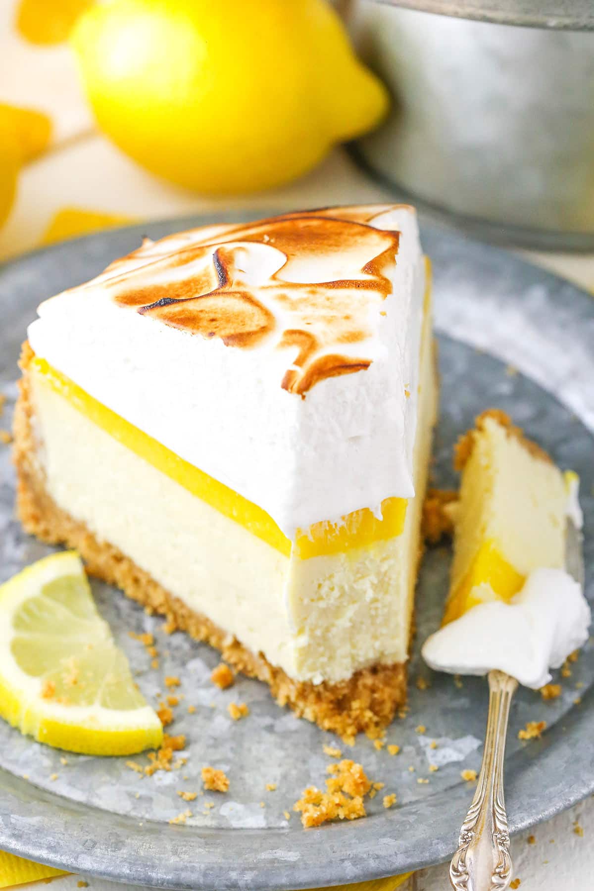 A slice of Lemon Meringue Cheesecake with a bite removed on a gray plate