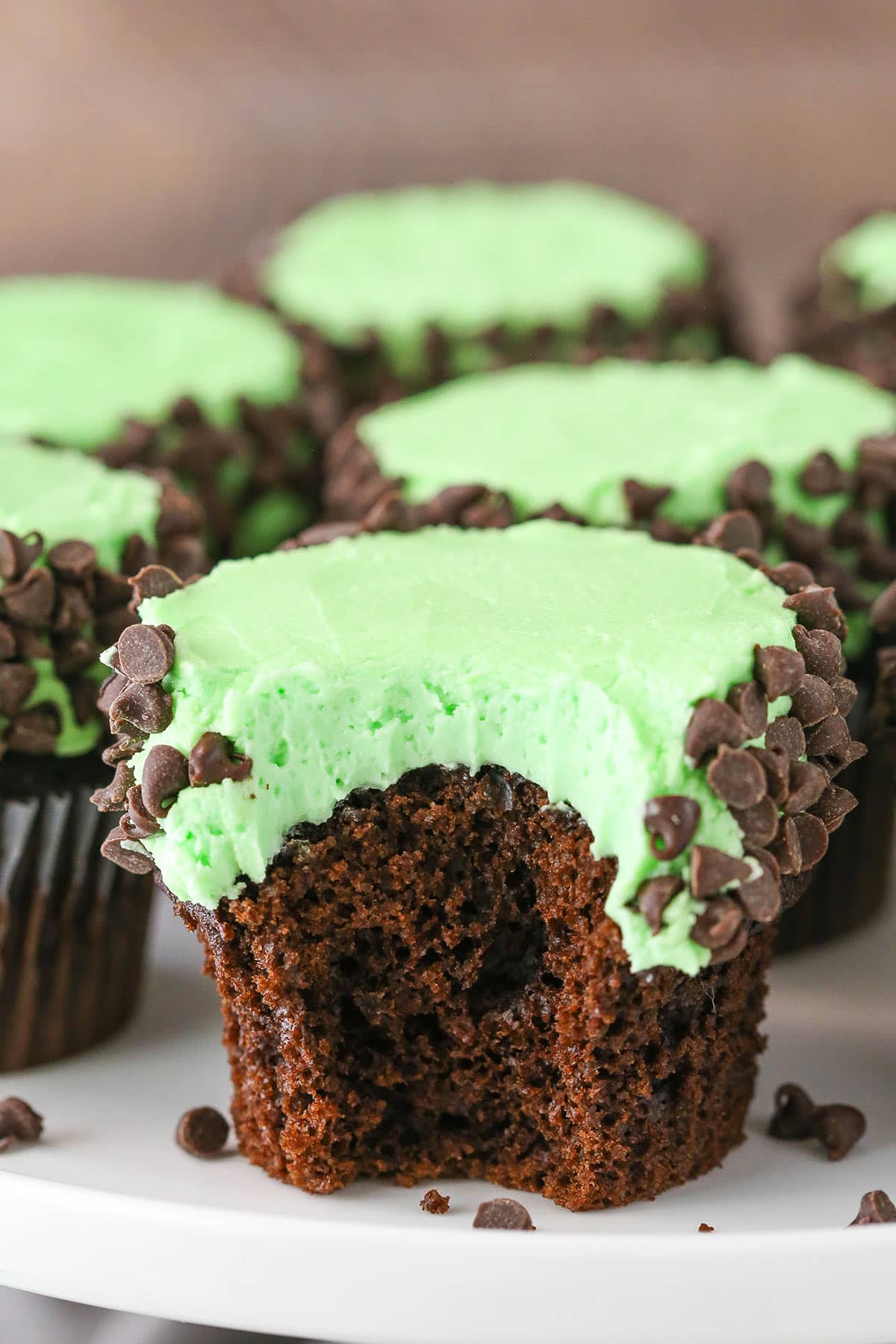 A Mint Chocolate Chip Cupcake with a bite removed on a white cake stand