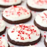 Several Peppermint Frosted Chocolate Cookies topped with candy cane bits on a flat surface.