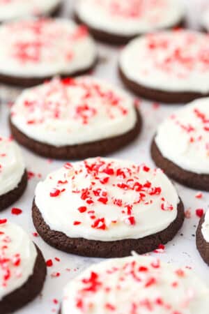 Several Peppermint Frosted Chocolate Cookies topped with candy cane bits on a flat surface.