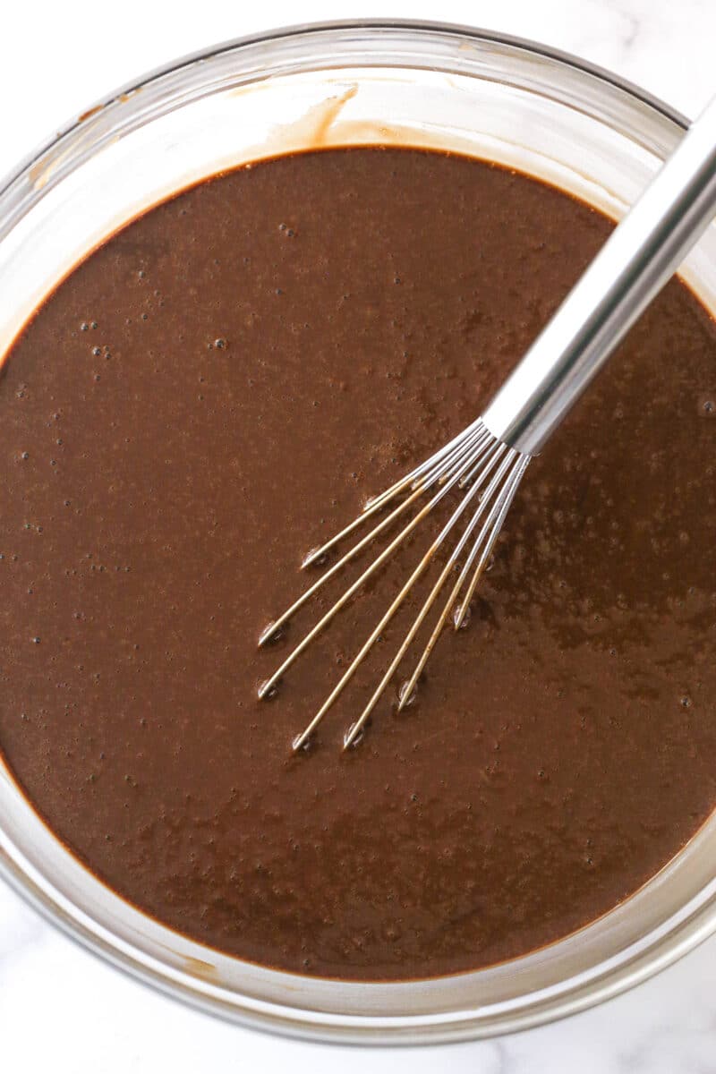 Batter for chocolate cake in a clear mixing bowl with a silver whisk.