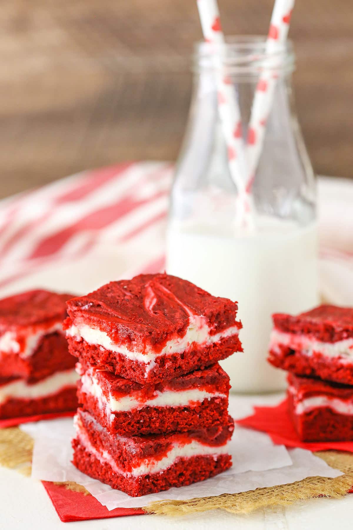 Three Red Velvet Cheesecake Swirl Brownies stacked on a white napkin with a bottle of milk in the background