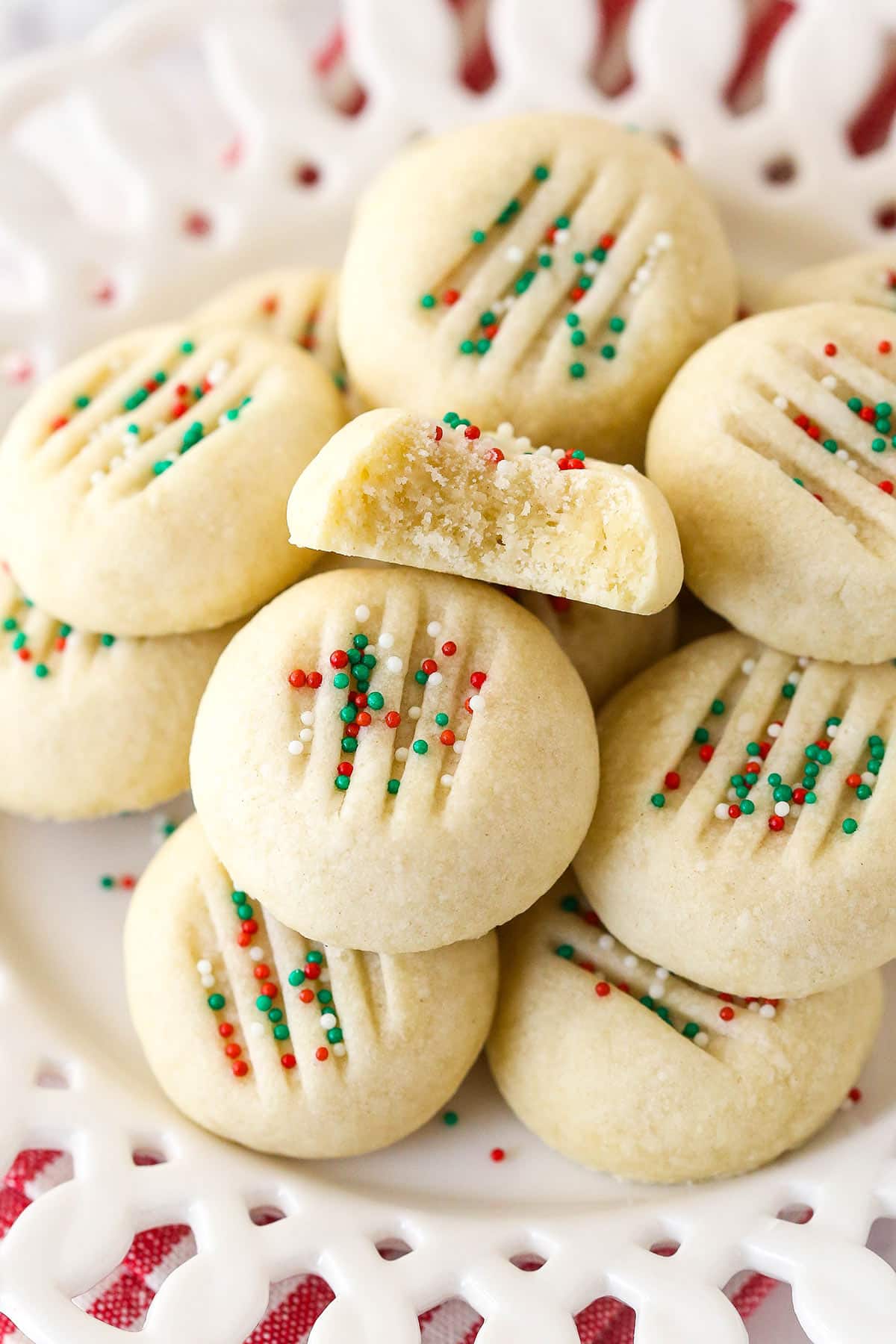 Overhead view of whipped shortbread cookies on a plate, one with a bite missing