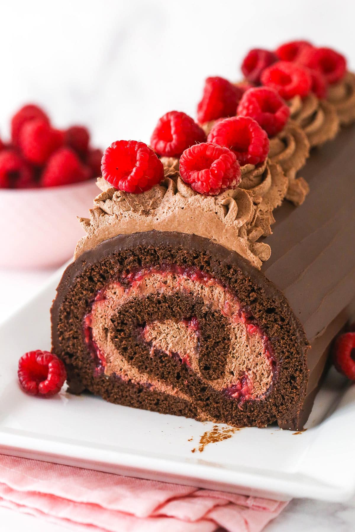 Raspberry chocolate swiss roll topped with raspberires on white platter