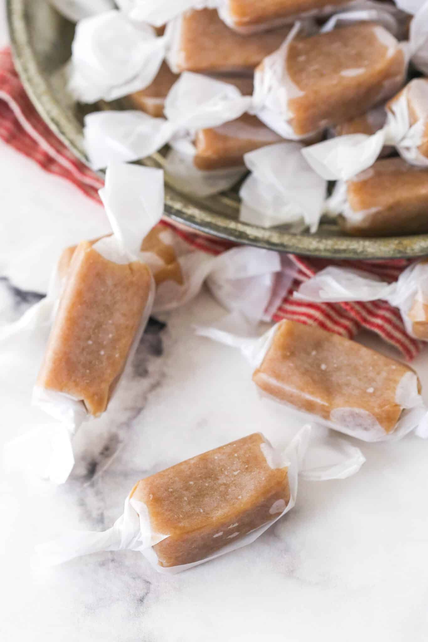 wrapped homemade caramels spilling out of dish onto marble countertop