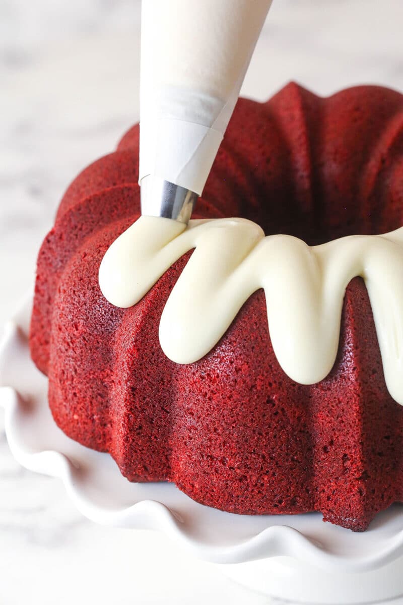 Piping cream cheese icing over red velvet bundt cake