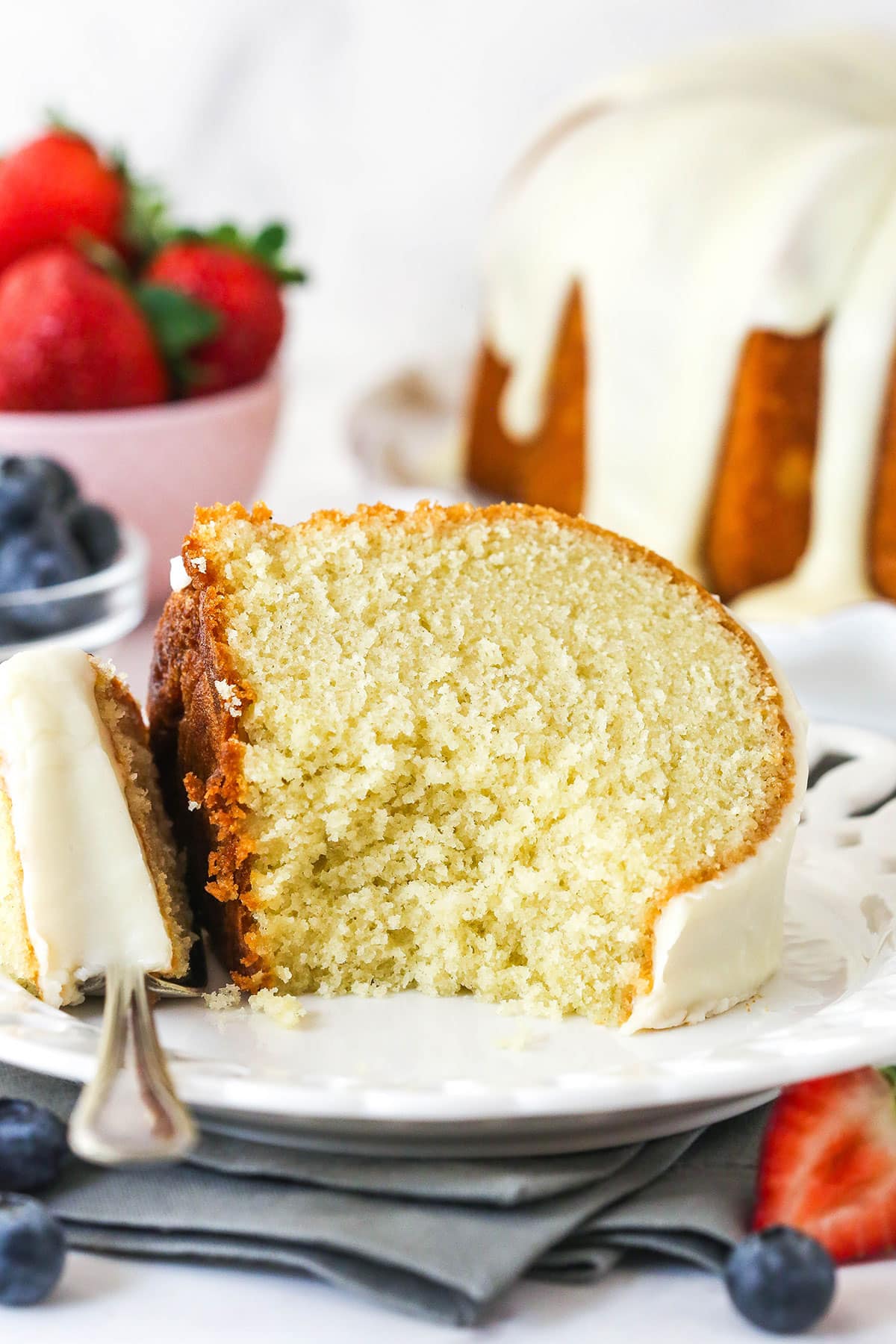 A slice of vanilla bundt cake on a white plate with a bite missing