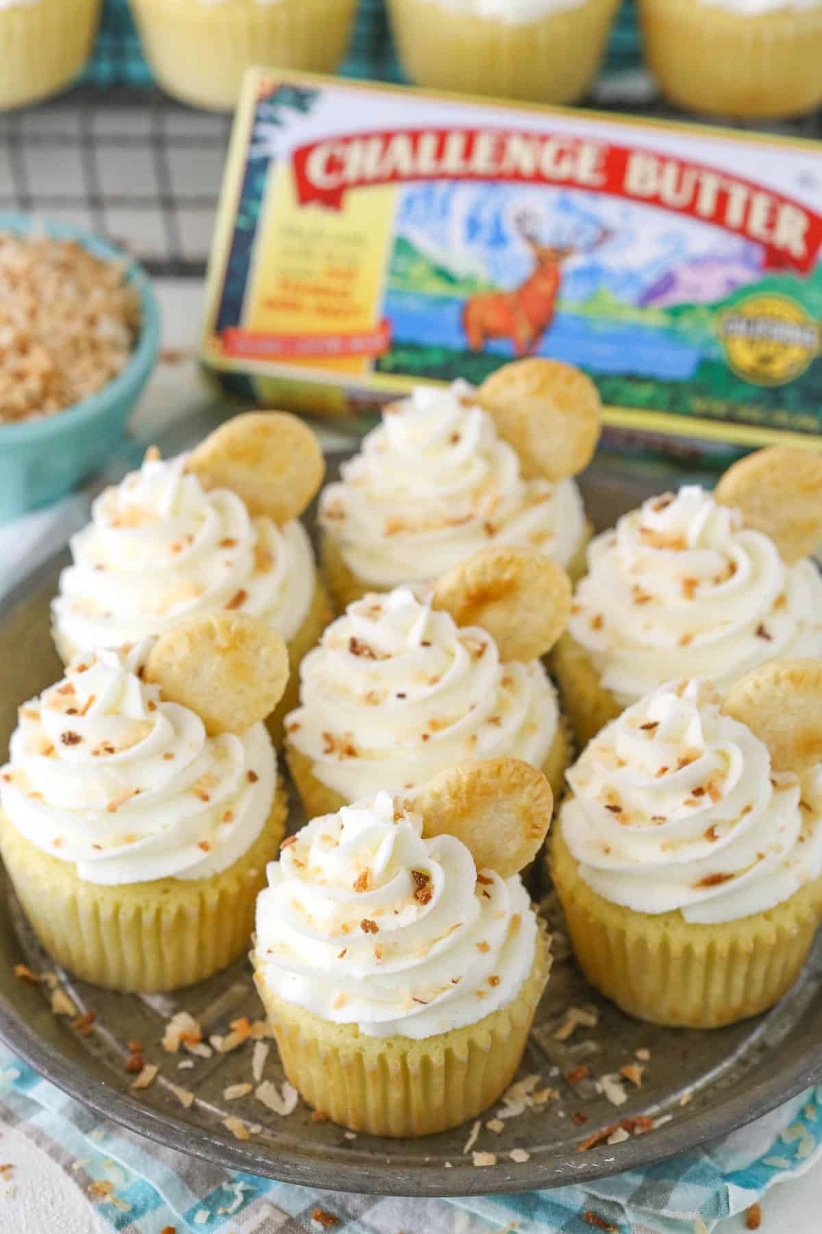 Top view of coconut cream pie cupcakes on a metal tray with a box of butter in the background.