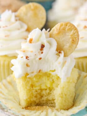 An unwrapped coconut cream pie cupcake with a bite taken out of it to show filling.