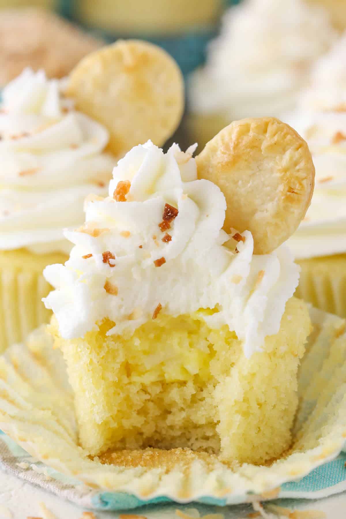 An unwrapped coconut cream pie cupcake with a bite taken out of it to show filling.