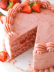 Homemade strawberry cake with a slice taken out of it near fresh strawberries.